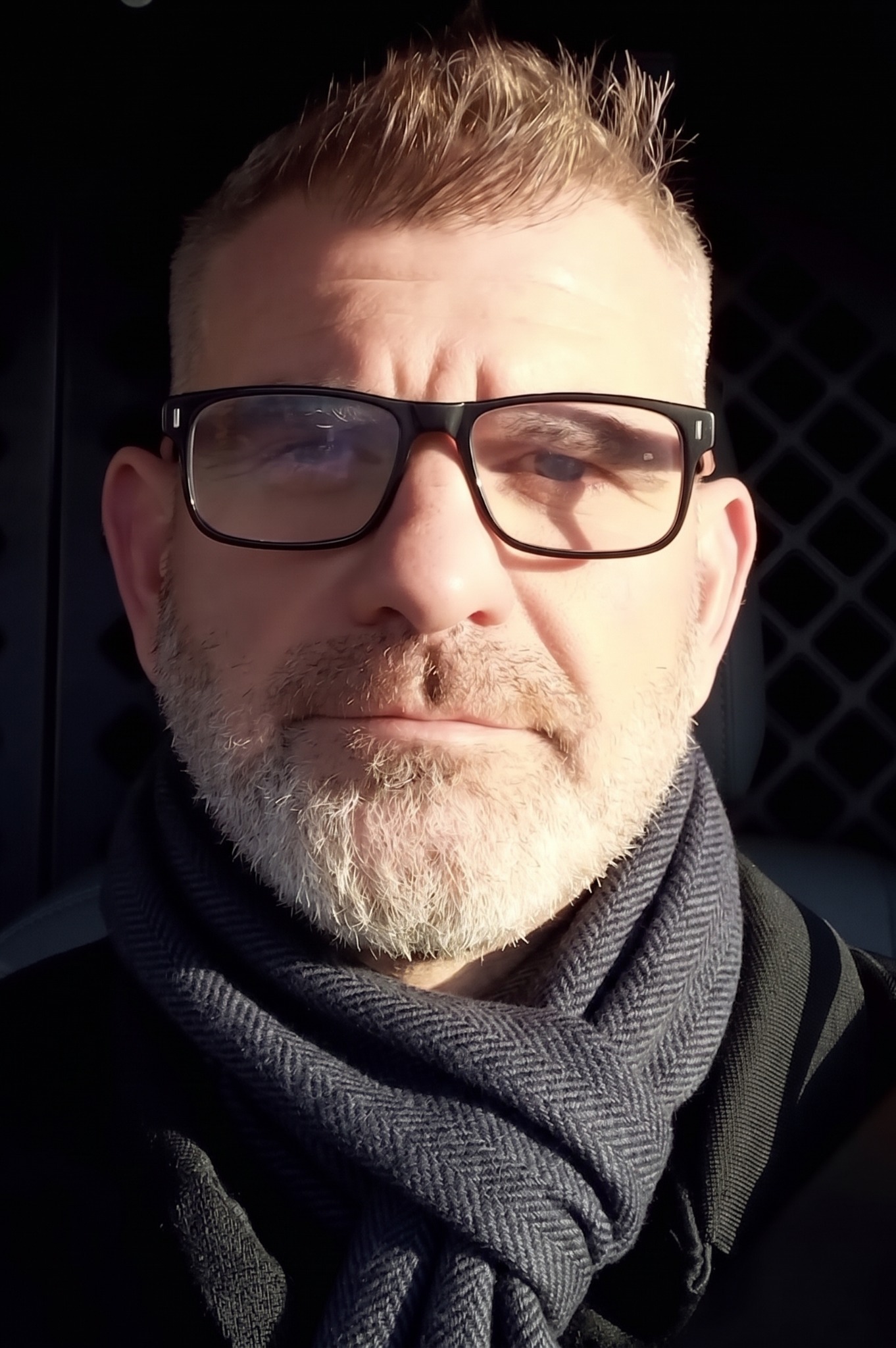 Tom Harwood in strong winter sunlight, wearing glasses and a dark scarf